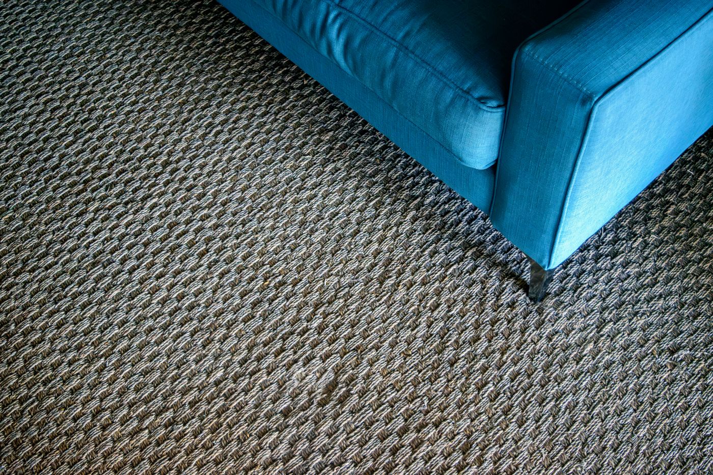 Blaues Sofa steht mit den Füßen auf einem grob gewebten Teppich